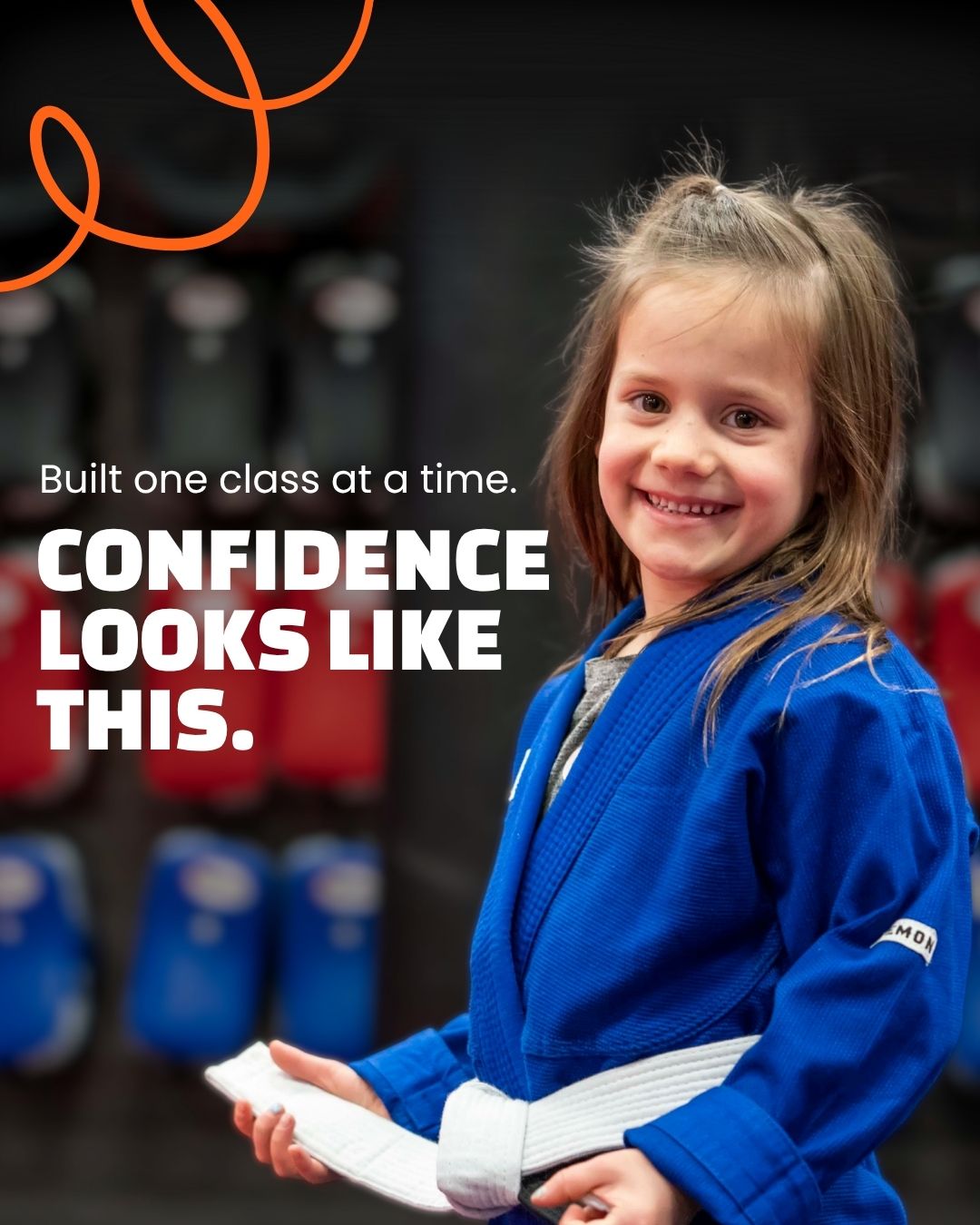 A young Champion's Creed student in a blue gi and white belt, smiling. Printed on the photo: Built one class at a time. Confidence looks like this.